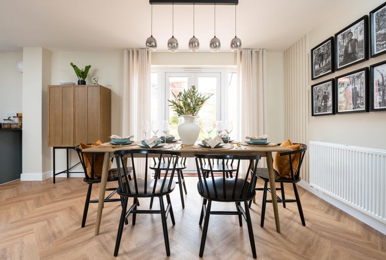 A dining room with a wooden table, chairs, and a vase of greenery.