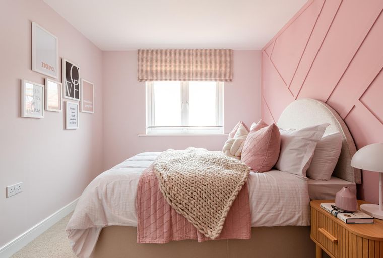 A bedroom with a bed, pillows, a throw blanket, framed art, a window, and a bedside table.