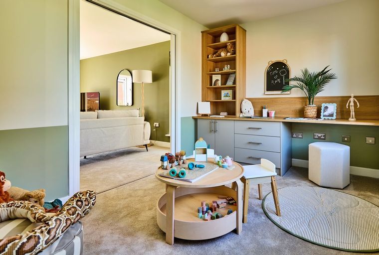 A children's playroom with a round play table, toy blocks, a bookshelf, and a desk.