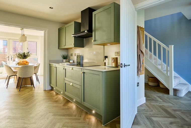A kitchen with green cabinets and a dining area next to it, with a staircase visible in the background.