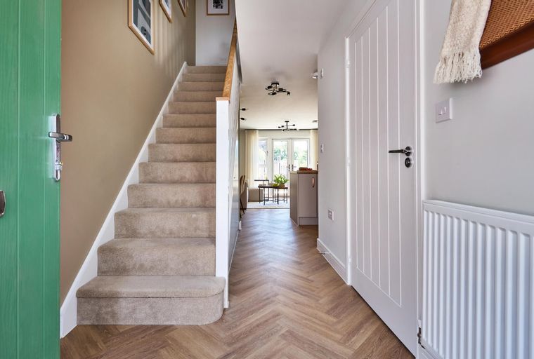 A hallway with a green front door, a carpeted staircase, and a herringbone floor.