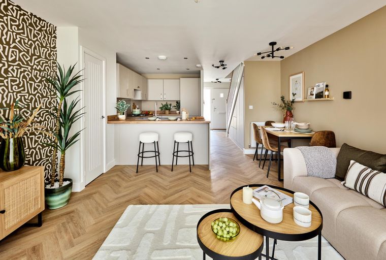 A living room and kitchen area with a dining table, sofa, kitchen island with stools, and herringbone flooring.