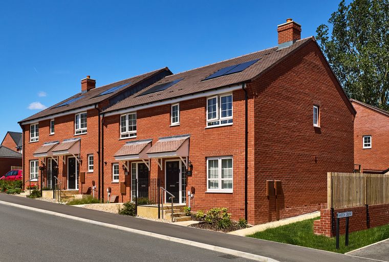 A row of modern red brick townhouses with solar panels on the roof and white-framed windows.