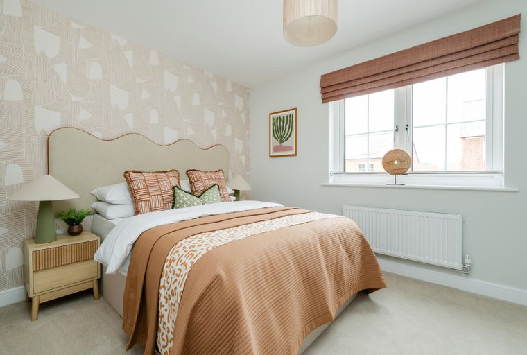 A bedroom with a bed, pillows, a bedside table, a lamp, and a window.