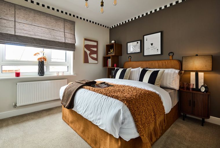 A bedroom with a bed, pillows, throws, and a bedside table.
