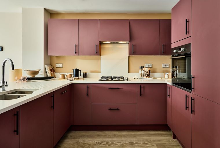 A modern kitchen with deep red cabinets, white countertops, and a gas stovetop.