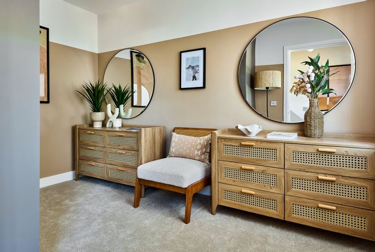 A hallway with two dressers, two mirrors, and a chair.