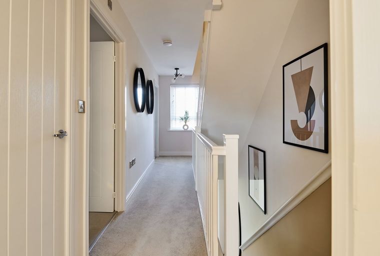 A hallway with a carpeted floor, a staircase, and doors.