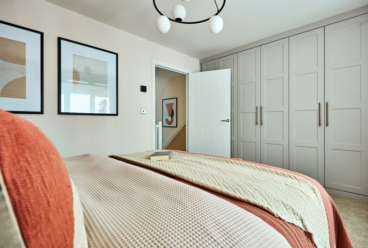 A bedroom with a bed, artwork, wardrobes, and an open doorway.