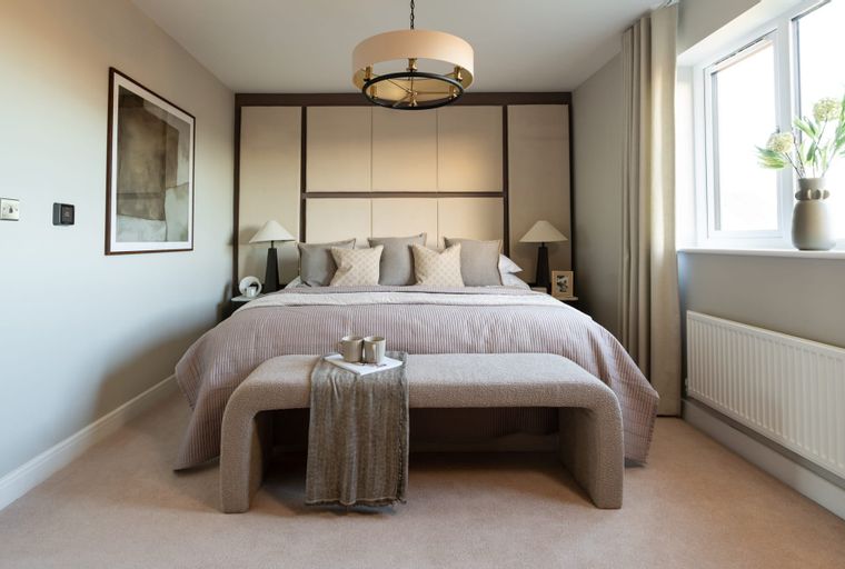 A bedroom with a bed, headboard, bedside tables, lamps, and a bench.