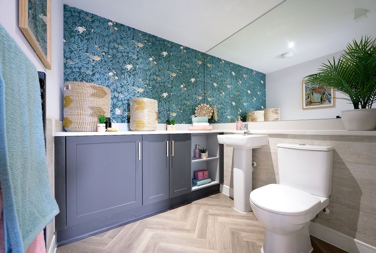 A bathroom with a toilet, sink, cabinetry, and patterned wallpaper.