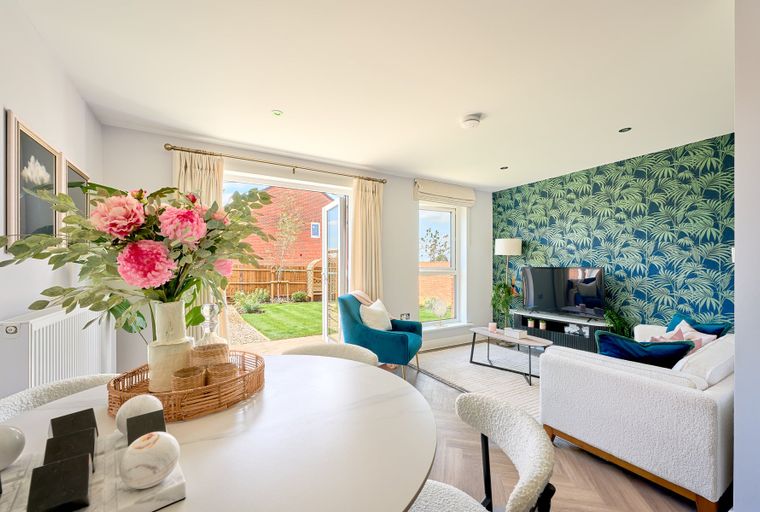 A living and dining room with a tropical wallpaper accent wall, French doors leading to a garden, and a dining table with chairs.