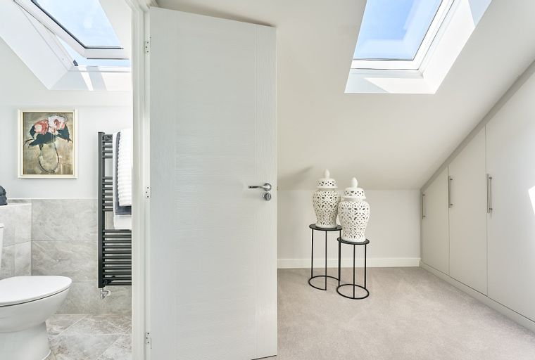 A bedroom with a bathroom, skylights, decorative vases, and built-in wardrobes.