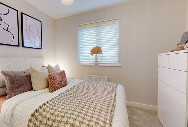 A bedroom with a bed, pillows, a throw blanket, a window, and a dresser.