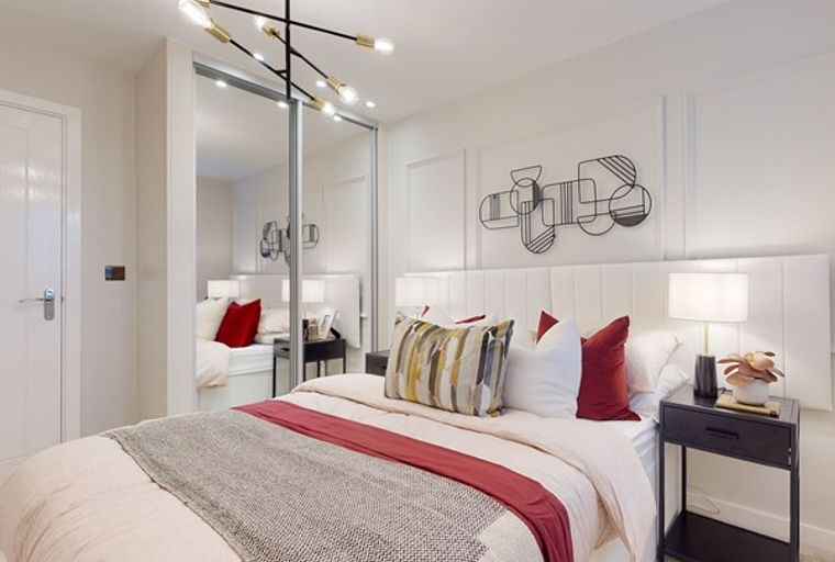 A bedroom with a bed, bedside table, lamp, and mirrored wardrobe.