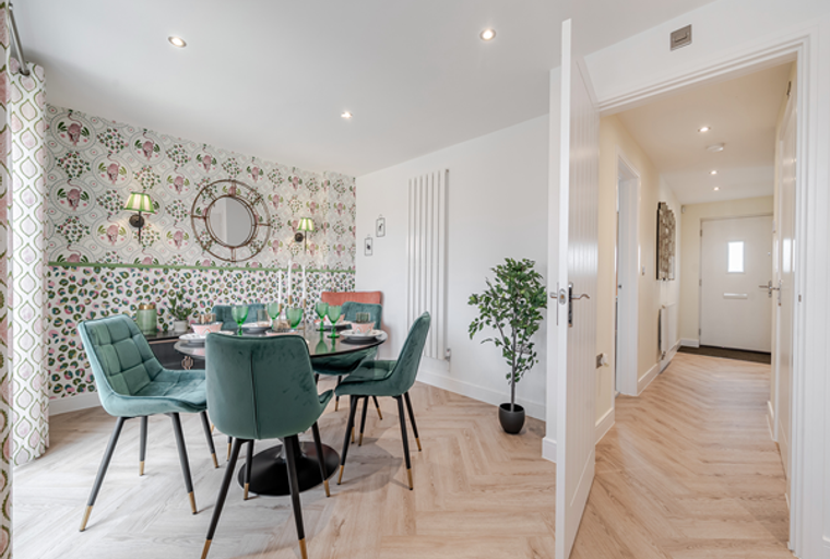 A dining room with a round table, teal chairs, patterned wallpaper, and wall sconces.