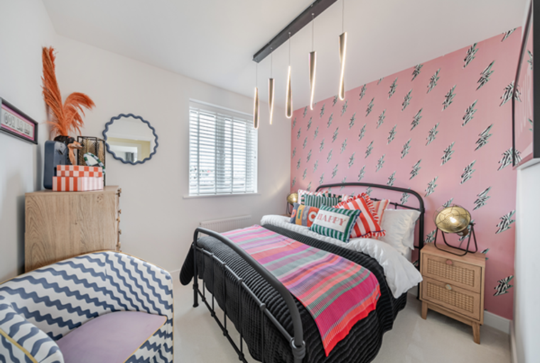 A bedroom with a bed, colorful pillows, and a patterned armchair.