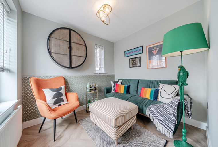 A living room with a green sofa, an orange chair, and a parrot floor lamp.