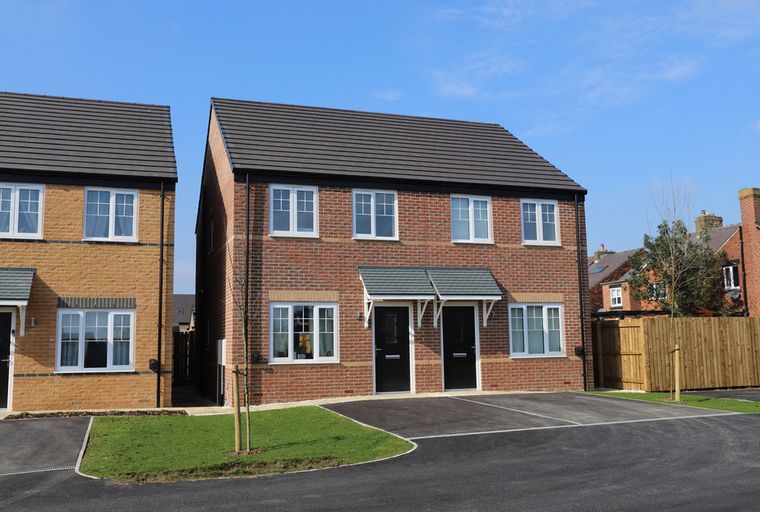 A pair of new semi-detached houses with brick exteriors and black front doors.