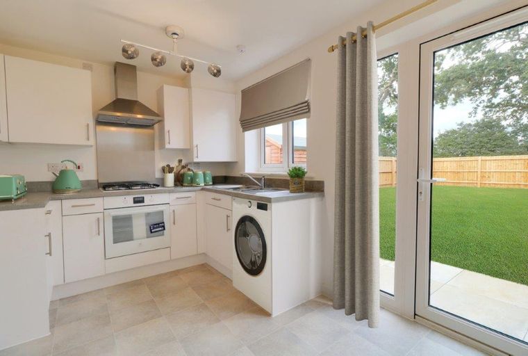 A kitchen with white cabinets, a stove, a sink, and a washing machine next to a door leading to a backyard.