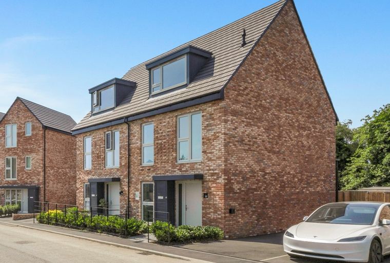 A row of modern brick townhouses with dormer windows and a white electric car parked in the driveway.