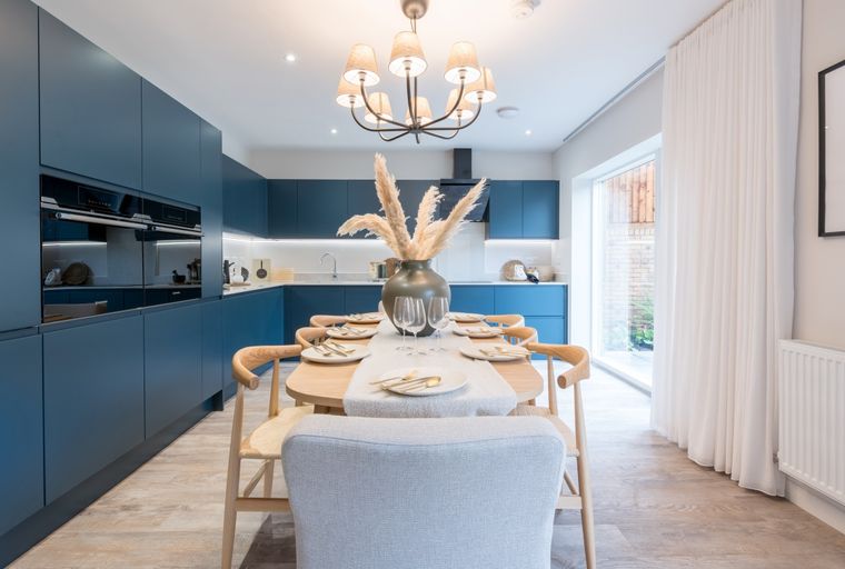 A dining area and kitchen with navy blue cabinets, a dining table set for a meal, and a chandelier.