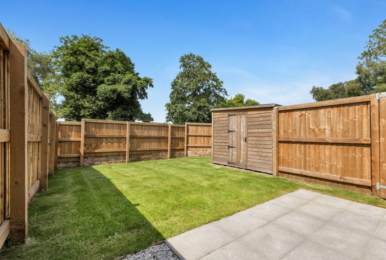 A backyard with a lawn, a wooden shed, a fence, and a paved patio.