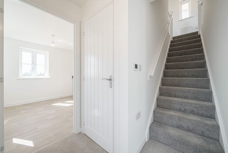 A hallway with a staircase and a doorway leading to a room with a window.