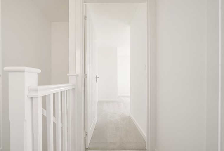 A hallway with a white railing and an open doorway.