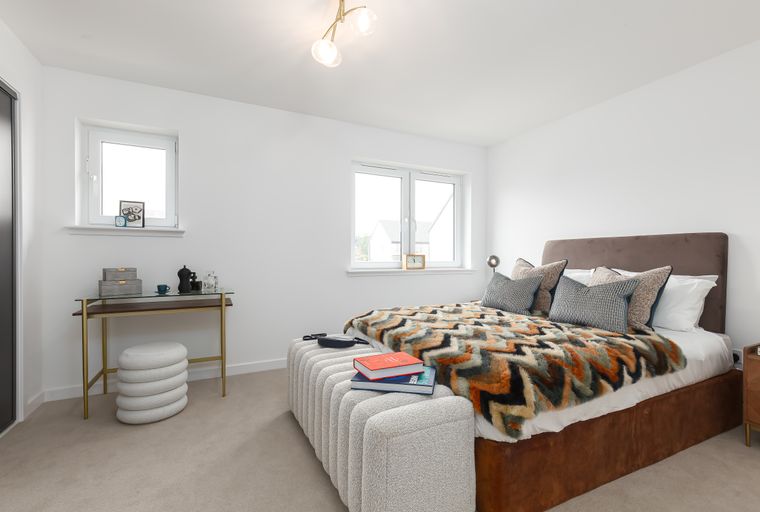 A bedroom with a bed, pillows, a throw blanket, windows, and a vanity table.