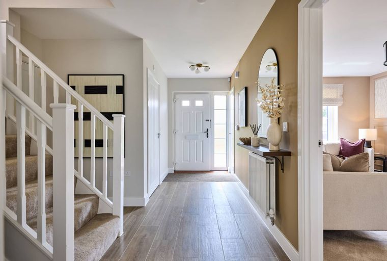 A hallway with a staircase, front door, and a console table with a mirror.