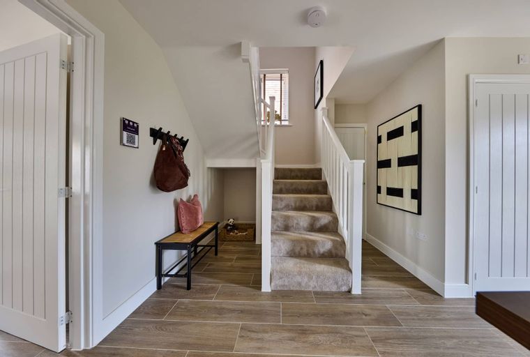 A hallway with a staircase, bench, and coat rack.