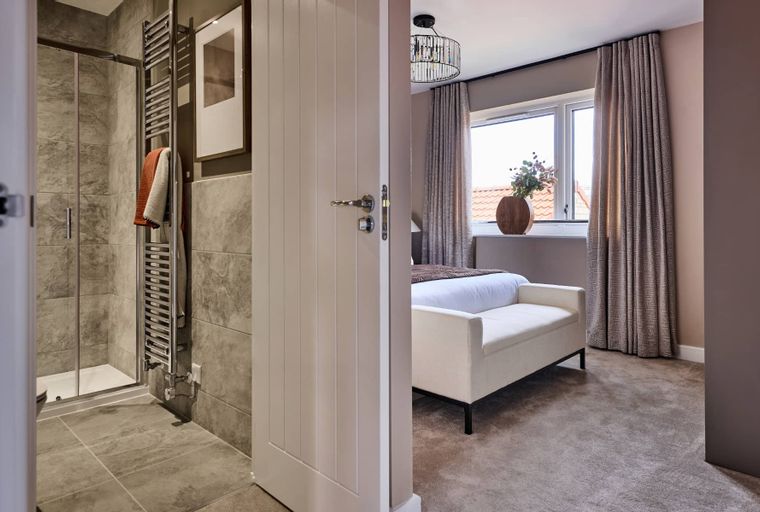 A bedroom and bathroom with a bed, bench, shower, and towel rail.