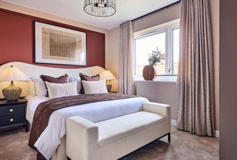 A bedroom with a bed, bedside tables, lamps, a bench, and a window with curtains.