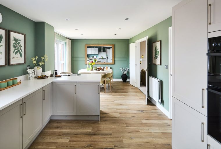 A kitchen and dining area with green walls, white countertops, and wooden floors.