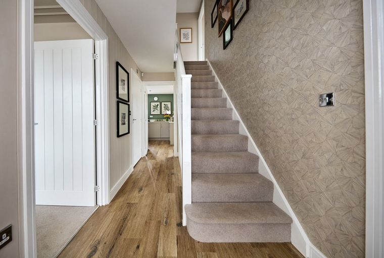 A hallway with a staircase, wood-effect flooring, and white doors.