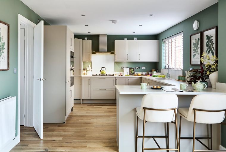 A modern kitchen with light wood flooring, sage green walls, and a breakfast bar.