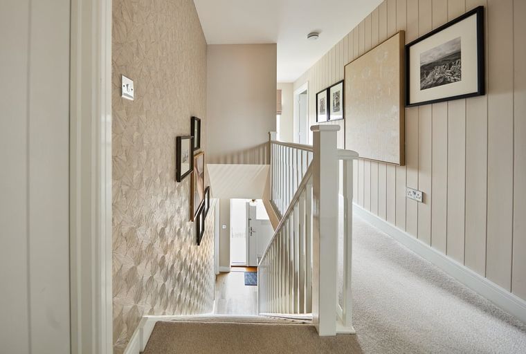 A hallway with a staircase and framed pictures on the wall.