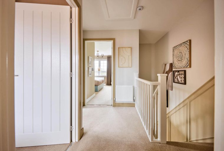 A hallway with a white paneled door, a carpeted landing, and a staircase with a white balustrade.