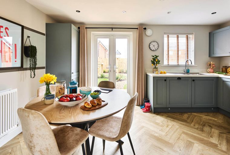 A kitchen and dining area with a round table, chairs, and a view of the garden through double doors.