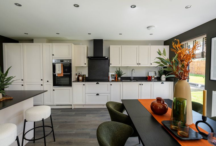 A modern kitchen and dining area with cream cabinets, a black backsplash, and a dining table with chairs.