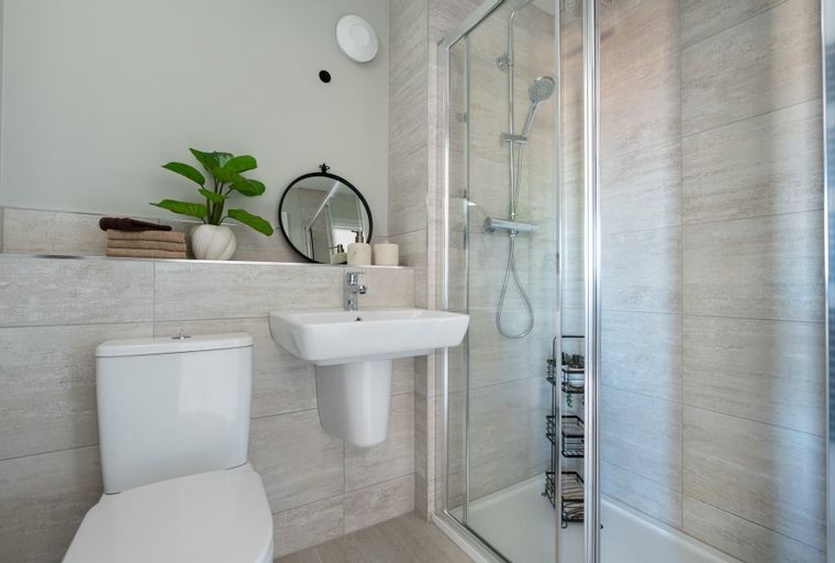 A bathroom with a toilet, sink, mirror, and shower.