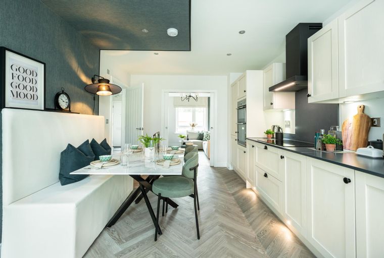 A dining area and kitchen with cream cabinets, a marble table, and green chairs.