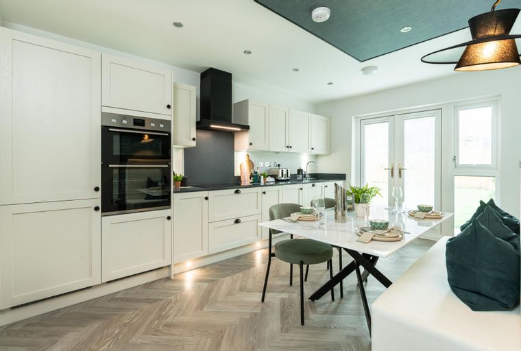 A modern kitchen and dining area with cream cabinets, a double oven, and a marble-top dining table.