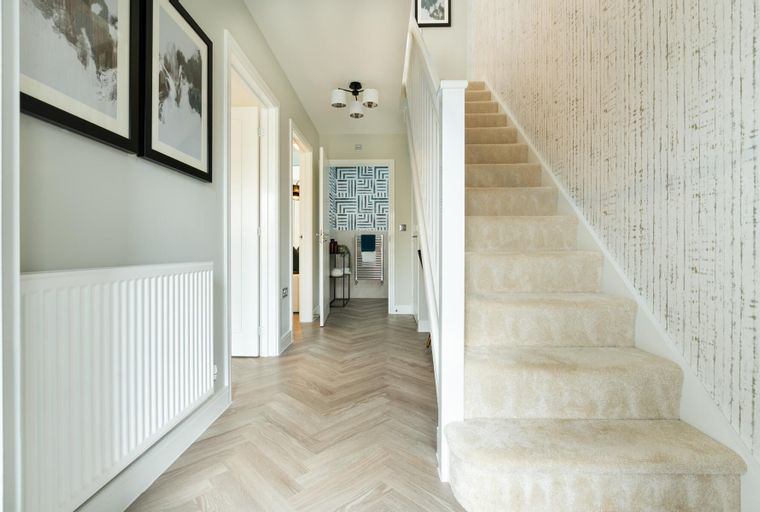 A hallway with a staircase, radiator, and artwork.