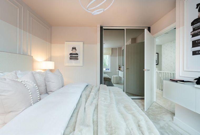 A bedroom with a bed, pillows, a blanket, a lamp, a framed picture, and a mirrored wardrobe.