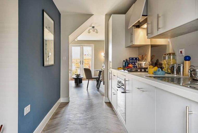 A kitchen and dining area with white cabinets, a gas hob, and a dining table near double doors leading to a garden.