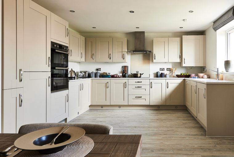 A modern kitchen with cream cabinets, integrated ovens, and a stainless steel extractor hood.