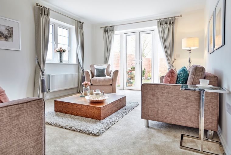 A living room with a sofa, armchair, coffee table, and French doors leading to a garden.