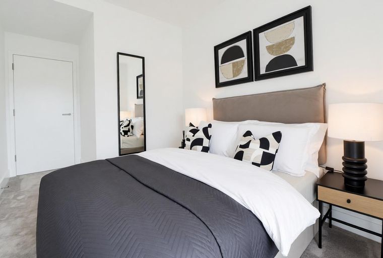 A bedroom with a bed, pillows, artwork, and a mirror.